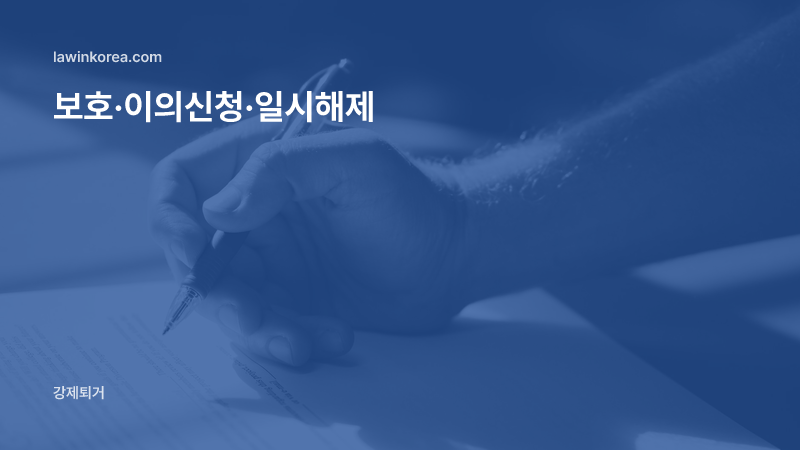 파란 펜으로 서류에 서명하는 손: 출입국 보호(구금)된 외국인, 이의신청·심사청구·일시해제는 어떻게 하나요?